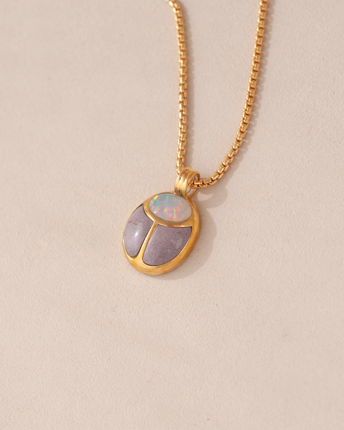 A gold vermeil necklace featuring a scarab amulet pendant with inlays of purple and white stones, displayed against a neutral background.