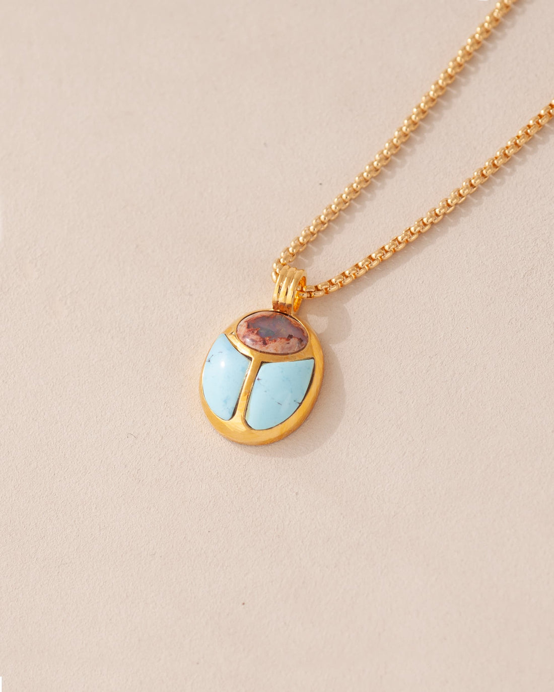 A gold vermeil necklace featuring a scarab amulet pendant with inlays of pink and blue stones, displayed against a neutral background.
