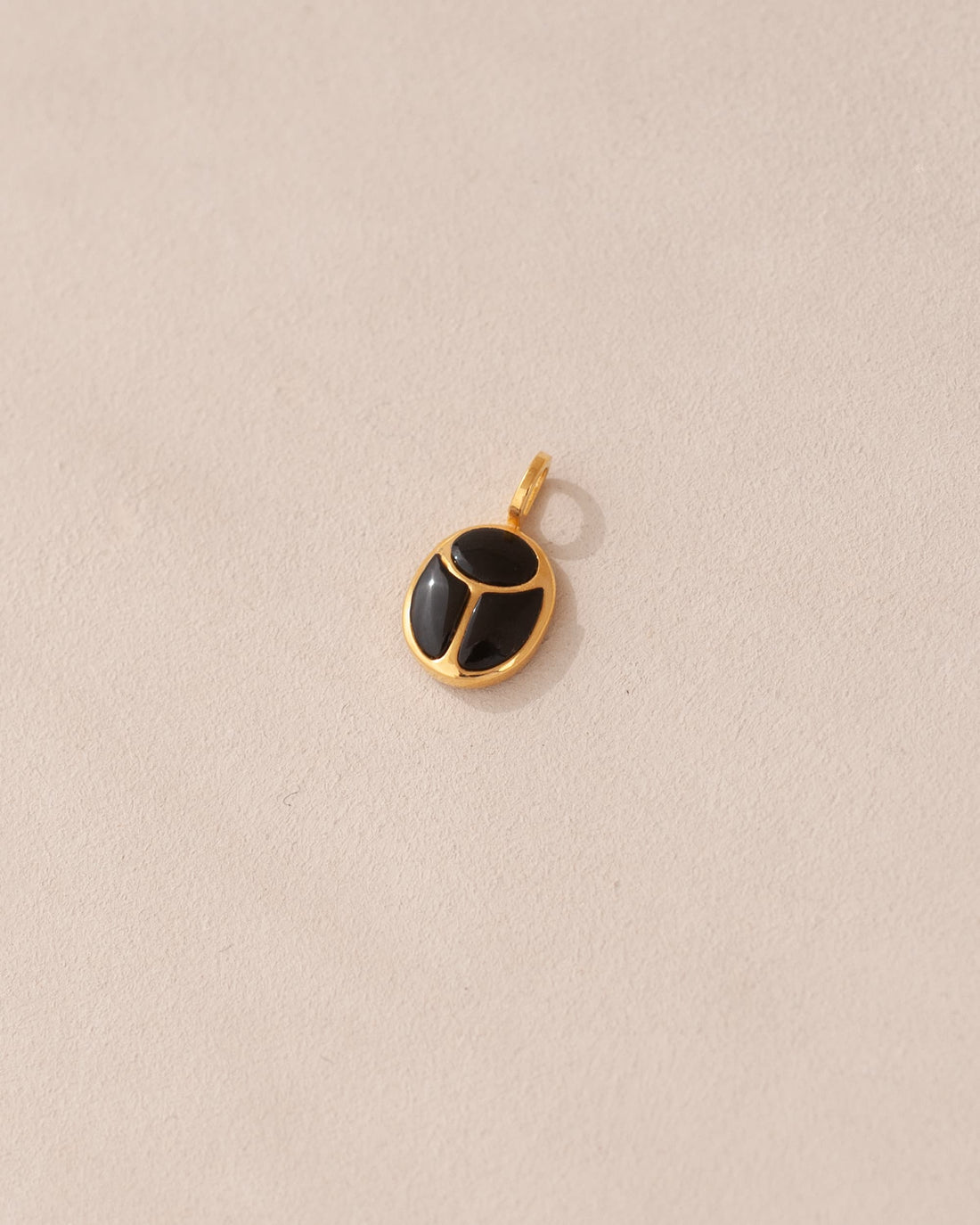 A gold charm featuring a scarab design with onyx inlays, displayed against a neutral background.