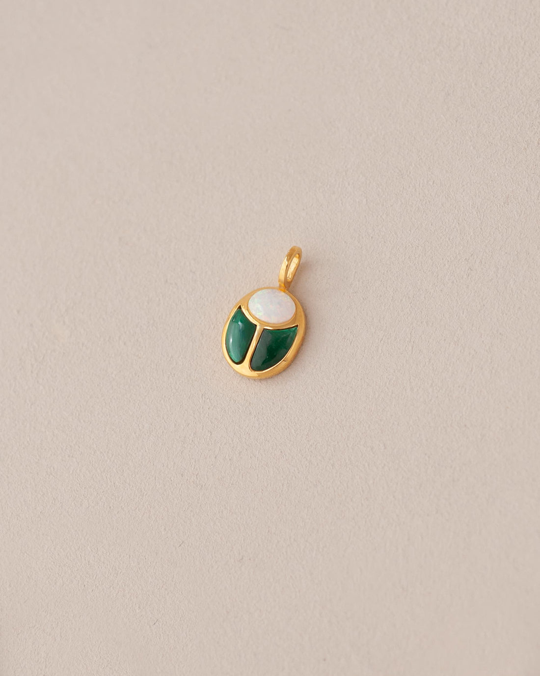 A gold charm featuring a scarab design with jelly opal and malachite inlays, displayed against a neutral background.