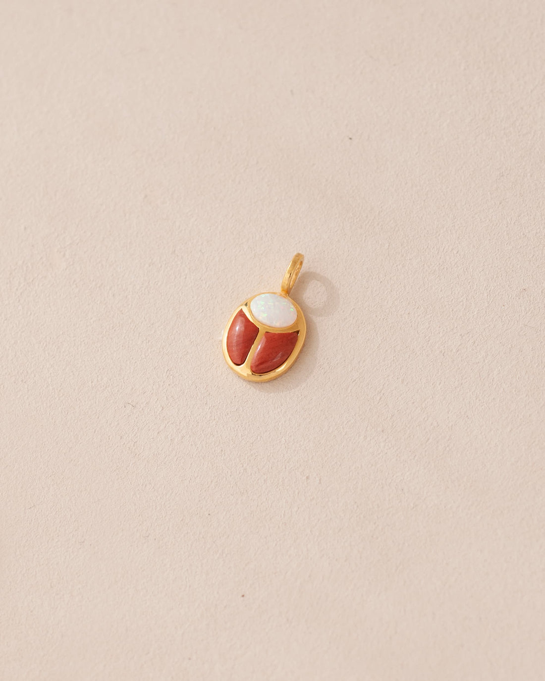 A small gold charm featuring a red jasper and opal scarab design.