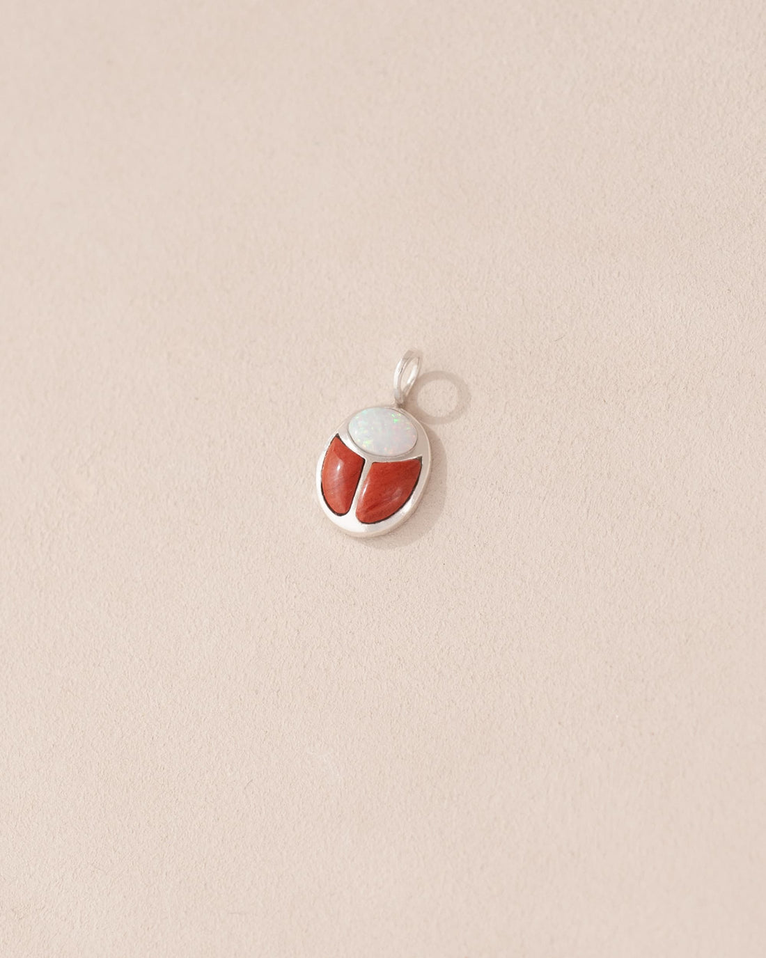 A small silver charm featuring a red jasper and opal scarab design.