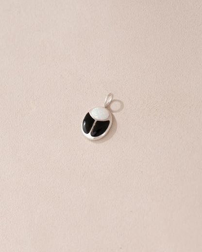 A small silver charm featuring a black and white stone, likely an onyx, designed to resemble a scarab amulet.