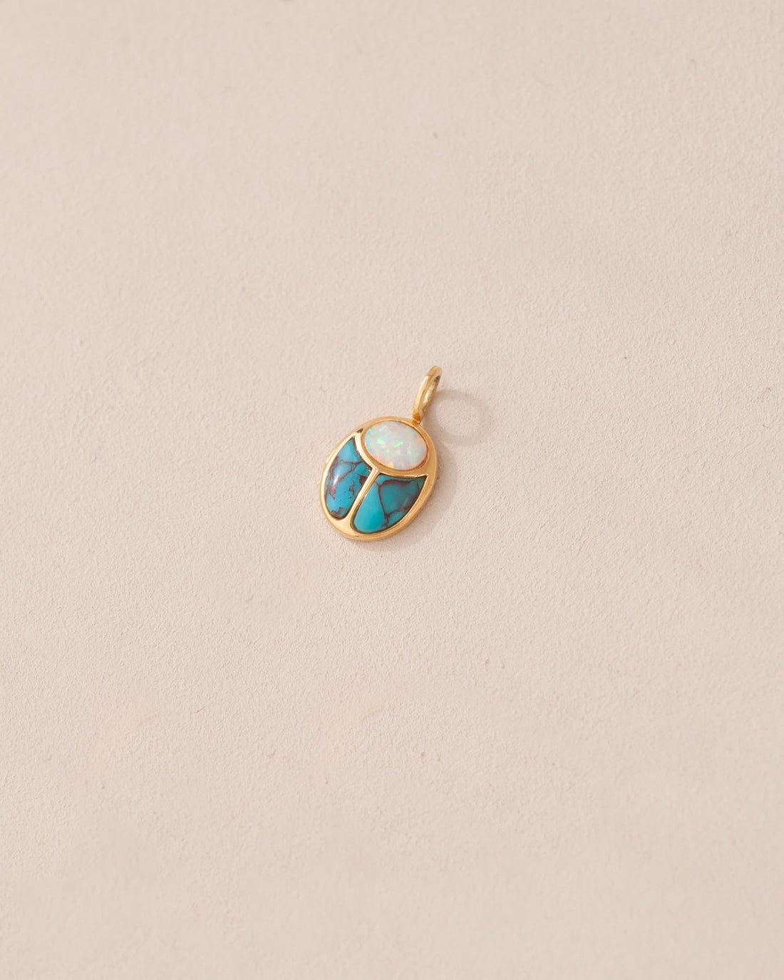 A small gold charm featuring a scarab design with opal and turquoise inlays, displayed against a neutral background.