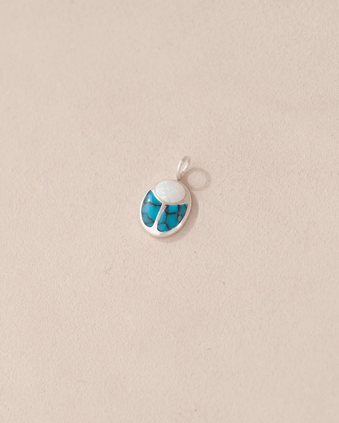 A small silver charm featuring a blue and white stone, designed to resemble a scarab amulet.