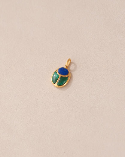 A gold charm featuring a scarab design with lapis lazuli and malachite inlays, displayed against a neutral background.