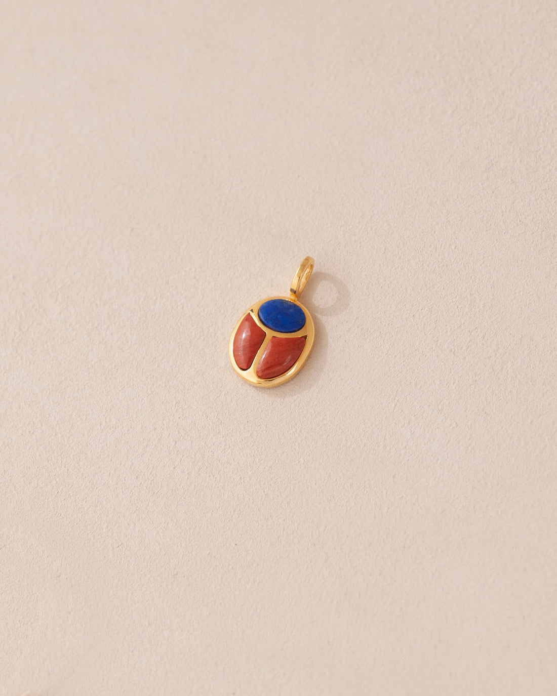 A gold charm featuring a scarab design with lapis lazuli and red jasper inlays, displayed against a neutral background.