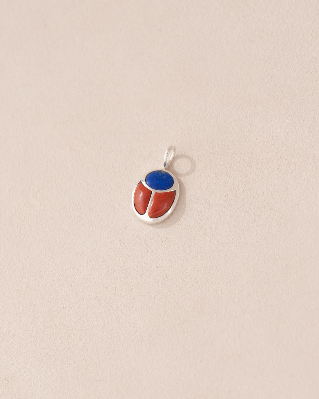 A silver-colored charm with a lapis lazuli and red jasper design, attached to a small silver chain.