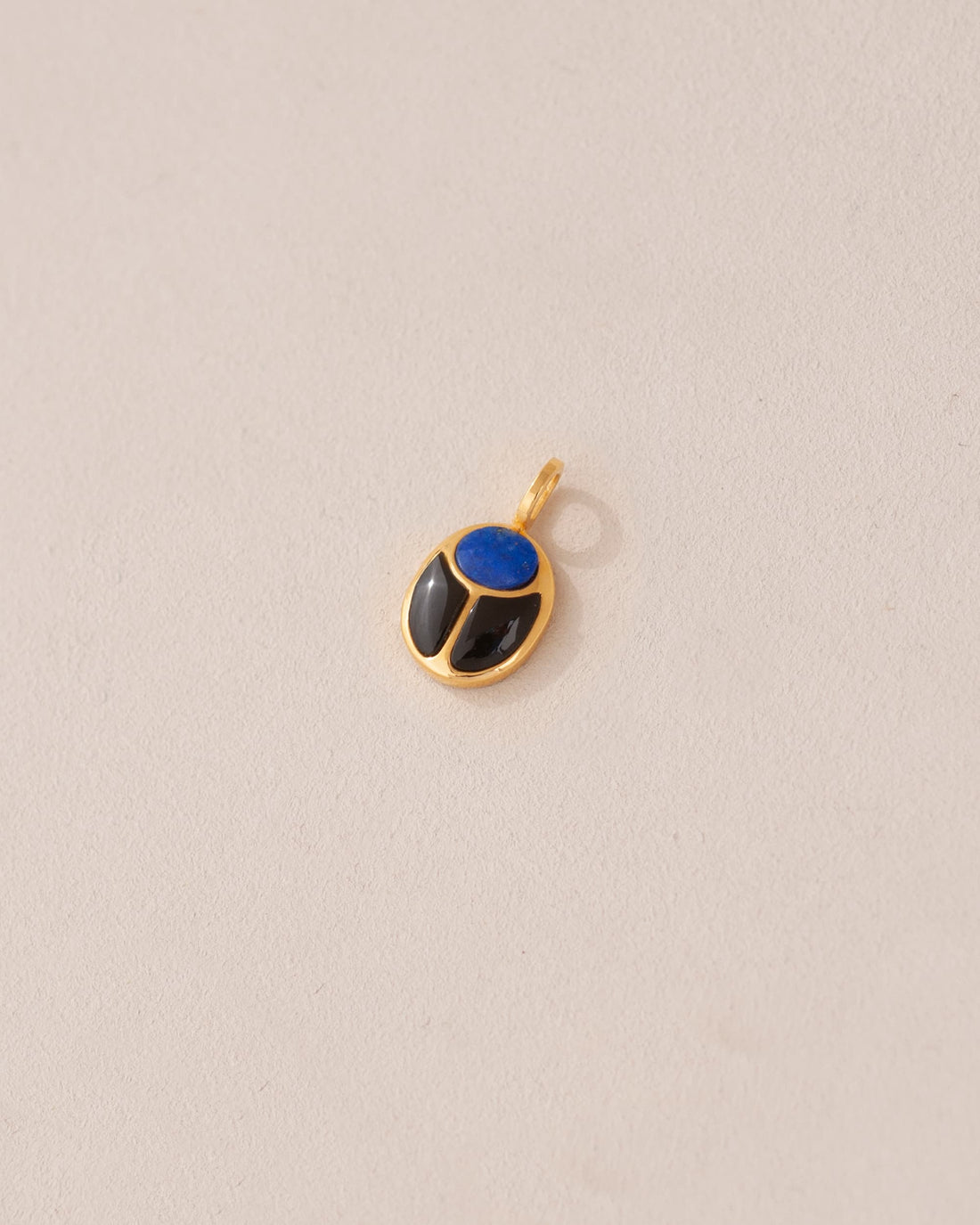 A gold charm featuring a scarab design with lapis lazuli and onyx inlays, displayed against a neutral background.