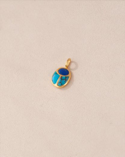 A gold charm featuring a lapis lazuli and turquoise scarab design.