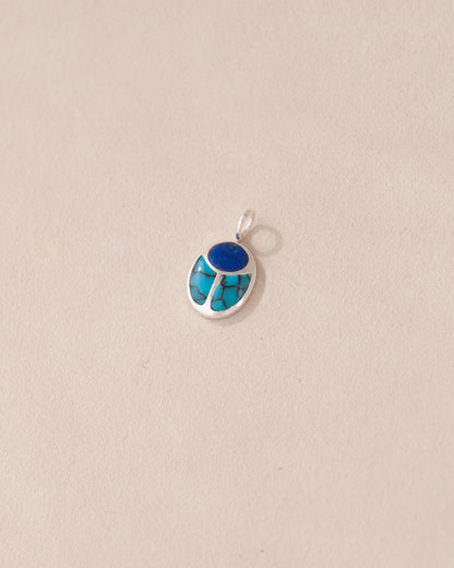 A silver charm featuring a small lapis lazuli and turquoise scarab design.