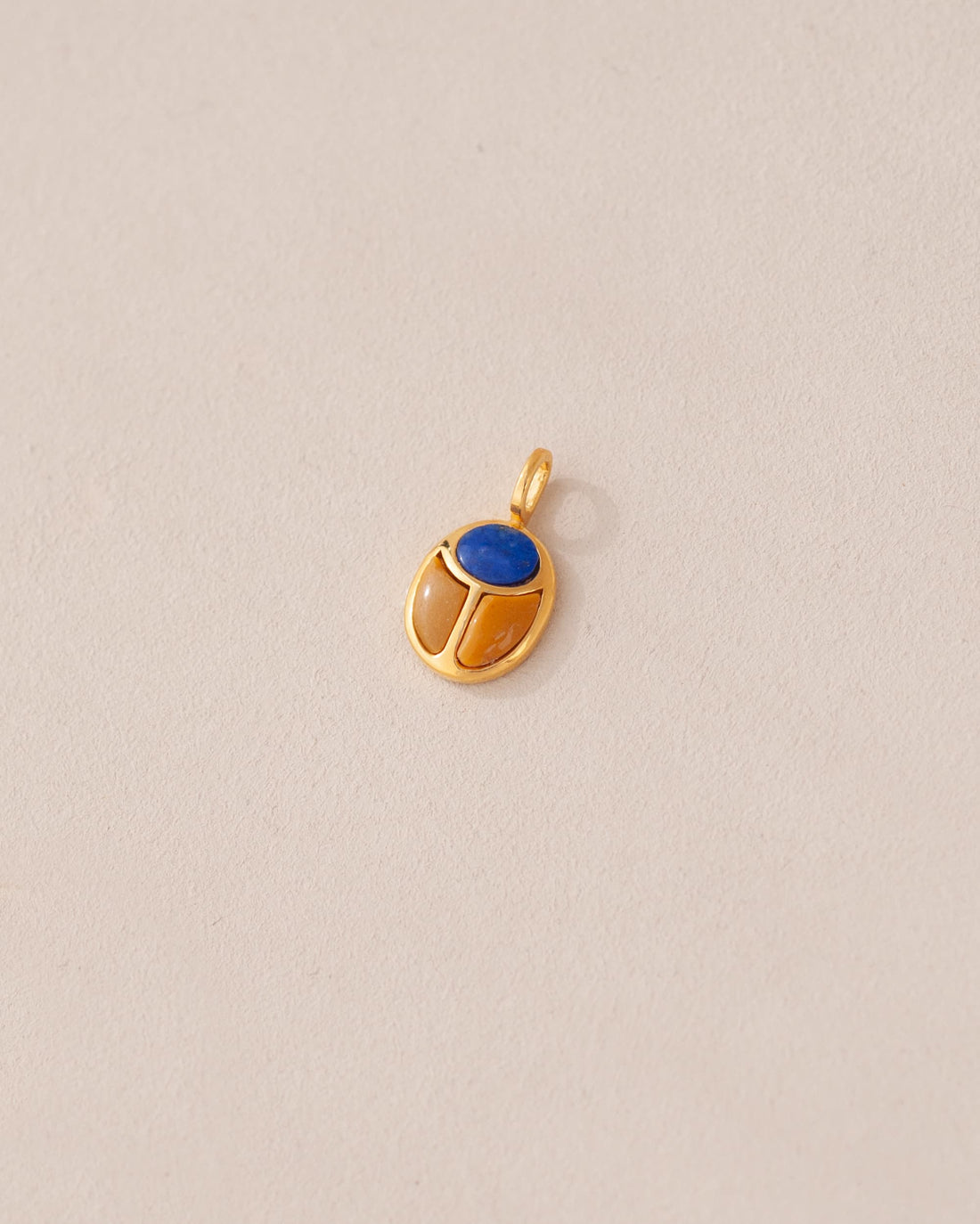 A gold charm featuring a scarab design with a blue lapis lazuli stone in the center, set against a neutral background.