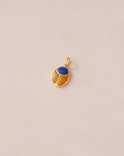 A gold charm featuring a scarab design with a blue lapis lazuli stone in the center, set against a neutral background.