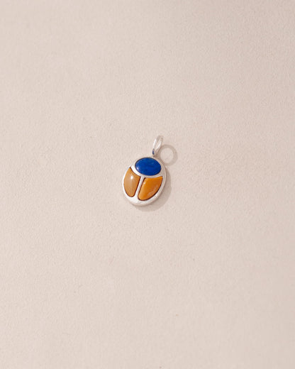 A silver-colored charm with a blue and orange design, possibly representing a scarab amulet.