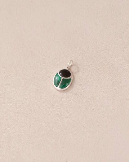 A silver charm with onyx and malachite colors, designed in the shape of a scarab amulet.