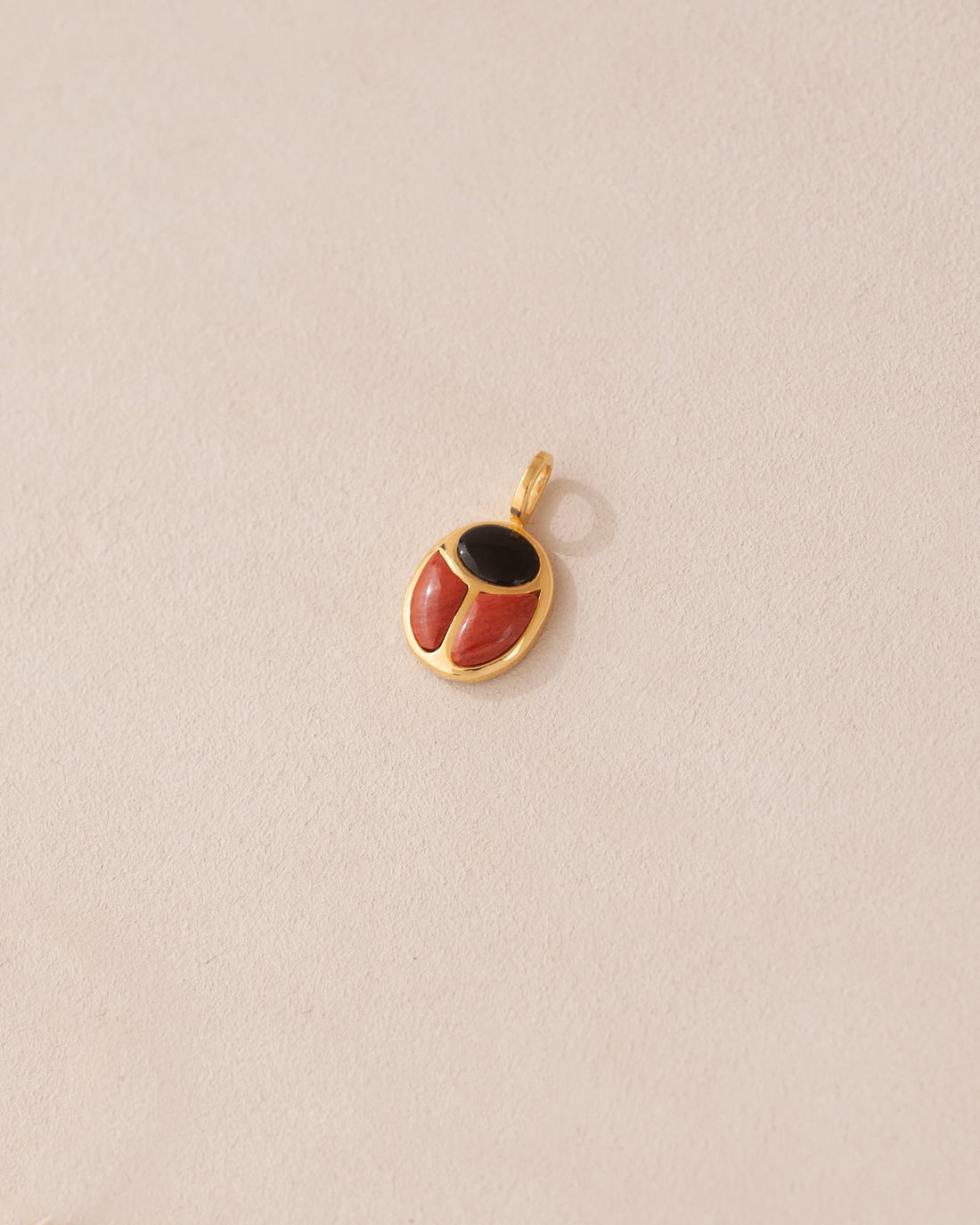 A gold charm featuring a scarab design with onyx and red jasper inlays, displayed against a neutral background.