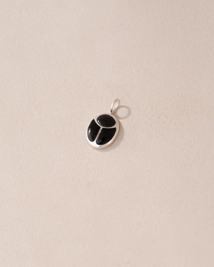 A silver-colored charm with an onyx-like black center, displayed against a beige background.
