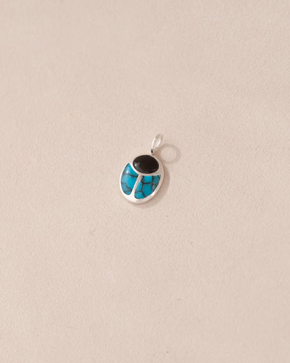 A small silver charm featuring a scarab design with onyx and turquoise inlays, displayed against a neutral background.