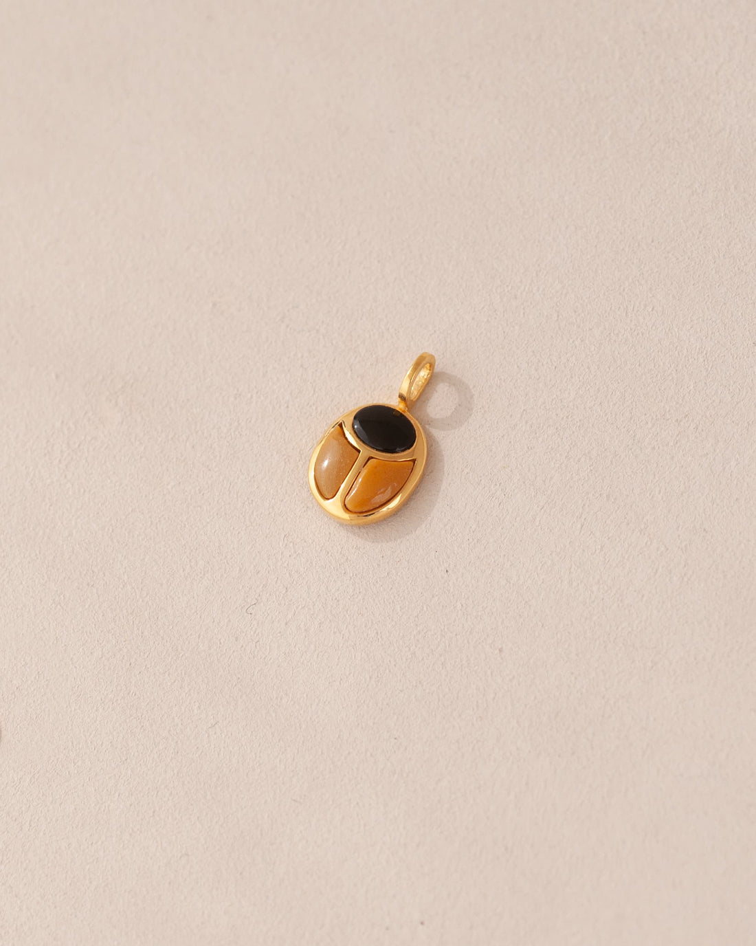 A gold charm featuring a scarab design with onyx and yellow opal inlays, displayed against a neutral background.