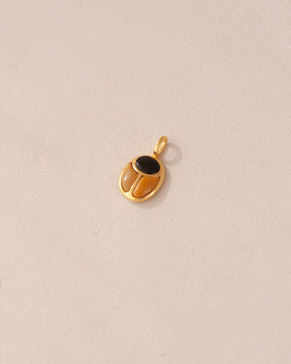 A gold charm featuring a scarab design with onyx and yellow opal inlays, displayed against a neutral background.