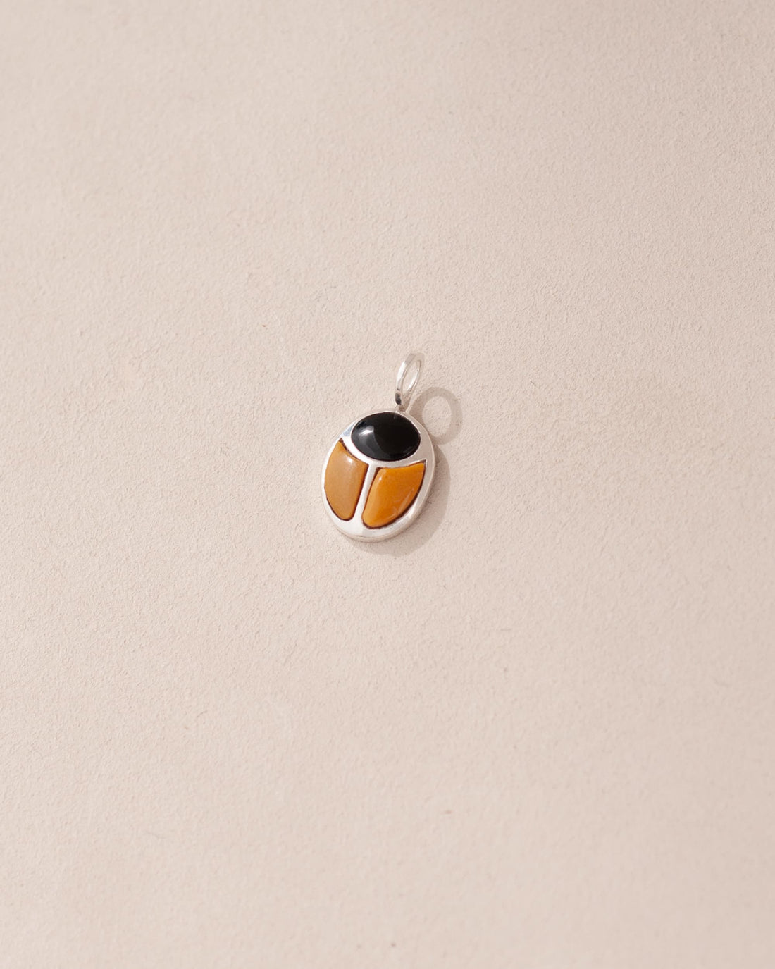 A silver-colored charm with an onyx and mookaite design, featuring a central onyx stone surrounded by a decorative border, against a beige background.