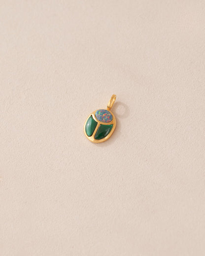 A gold charm featuring a scarab design with starry opal and malachite inlays, displayed against a neutral background.
