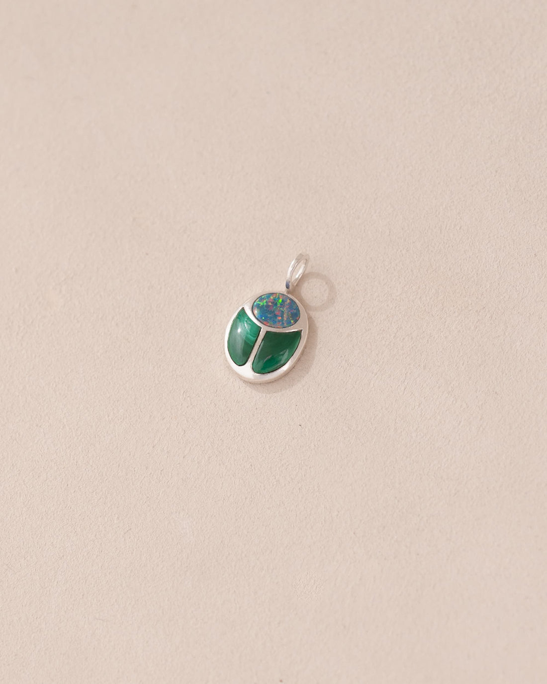 A silver charm with starry opal and malachite designs, against a beige background.