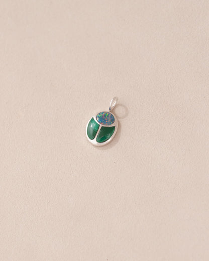 A silver charm with starry opal and malachite designs, against a beige background.
