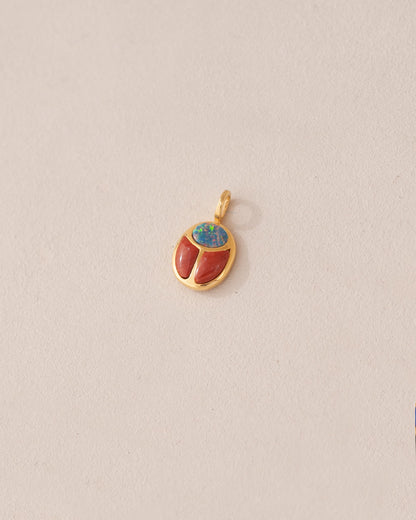 A small gold charm featuring a red jasper and opal scarab design.