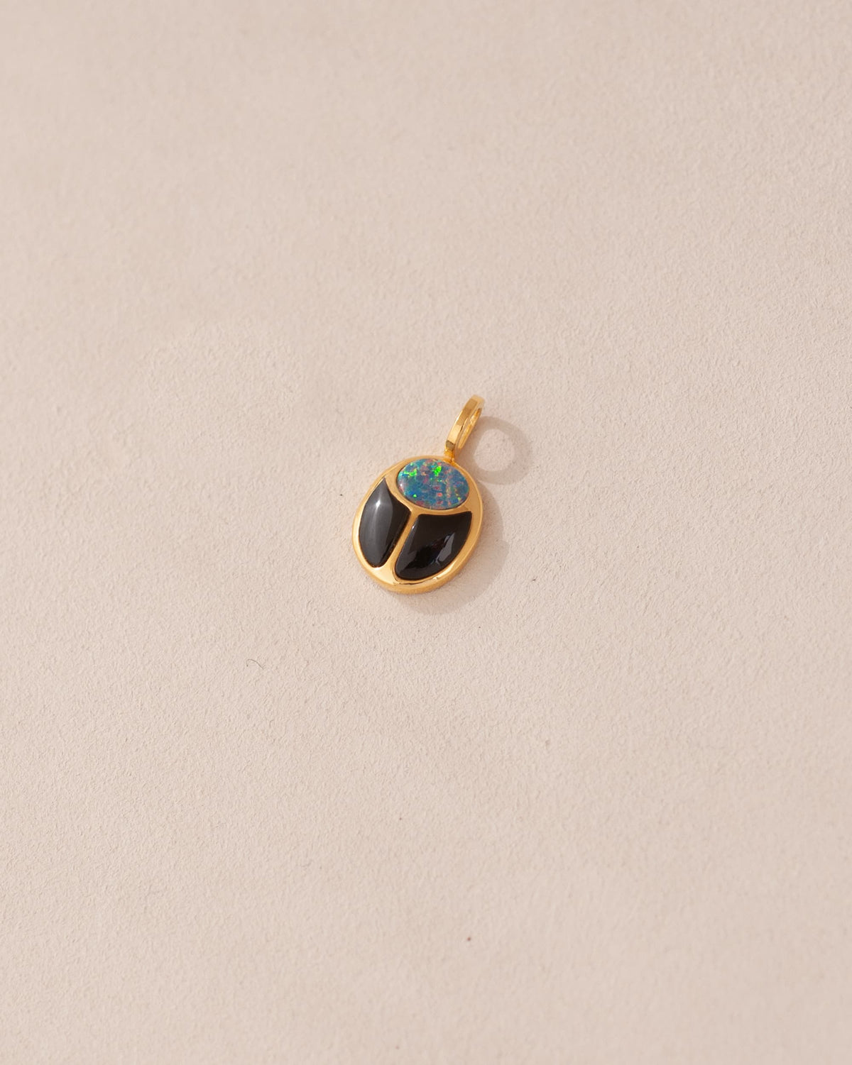 A 14K yellow gold charm featuring a starry opal and onyx design, resembling a scarab amulet.