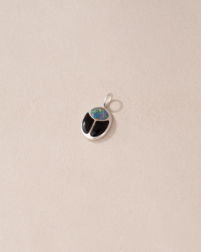 A small silver charm featuring a starry opal and onyx design, shaped like a scarab amulet.