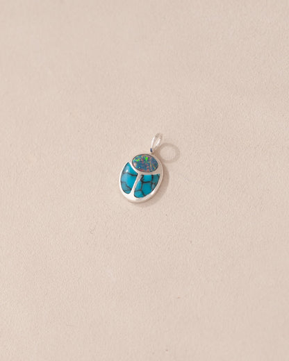 A silver charm featuring a starry opal and turquoise scarab design.