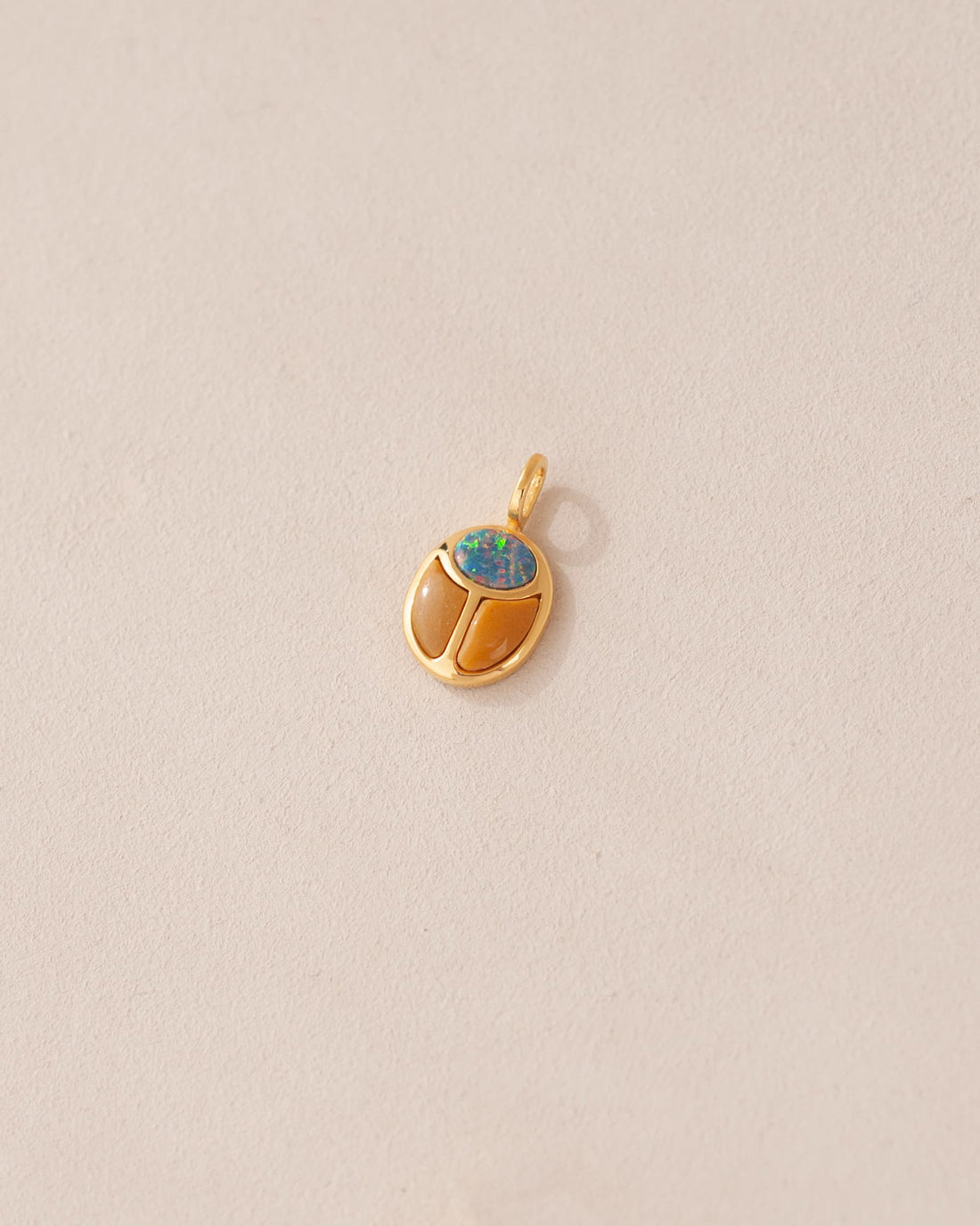 A gold-colored charm with a starry opal and mookaite design, resembling a scarab amulet, against a light background.