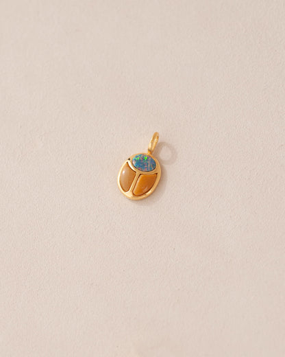 A gold-colored charm with a starry opal and mookaite design, resembling a scarab amulet, against a light background.