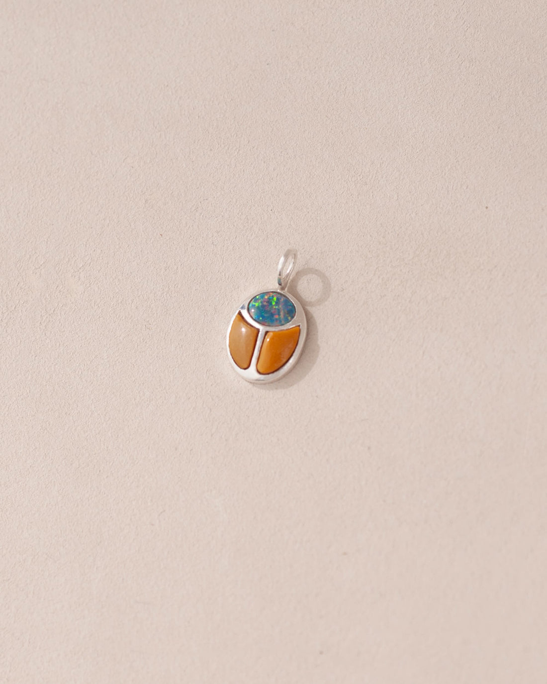 A silver charm featuring a starry opal and mookaite design, shaped like a scarab amulet, displayed against a neutral background.