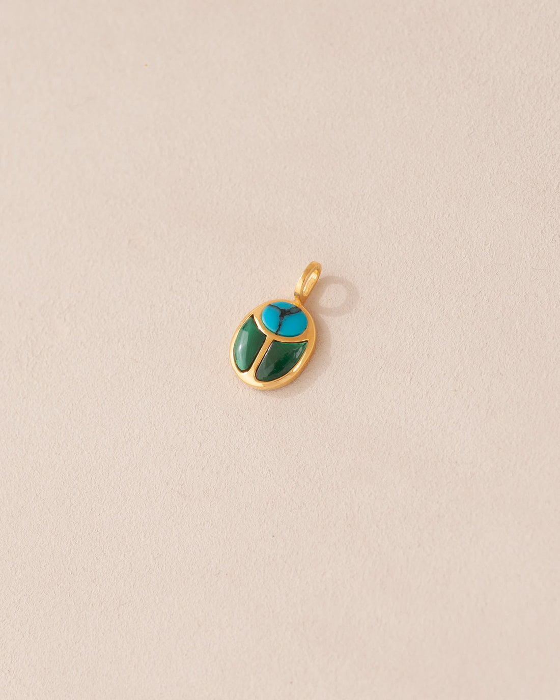 A small turquoise and malachite stone charm in a gold setting, shaped like a scarab, displayed against a light background.