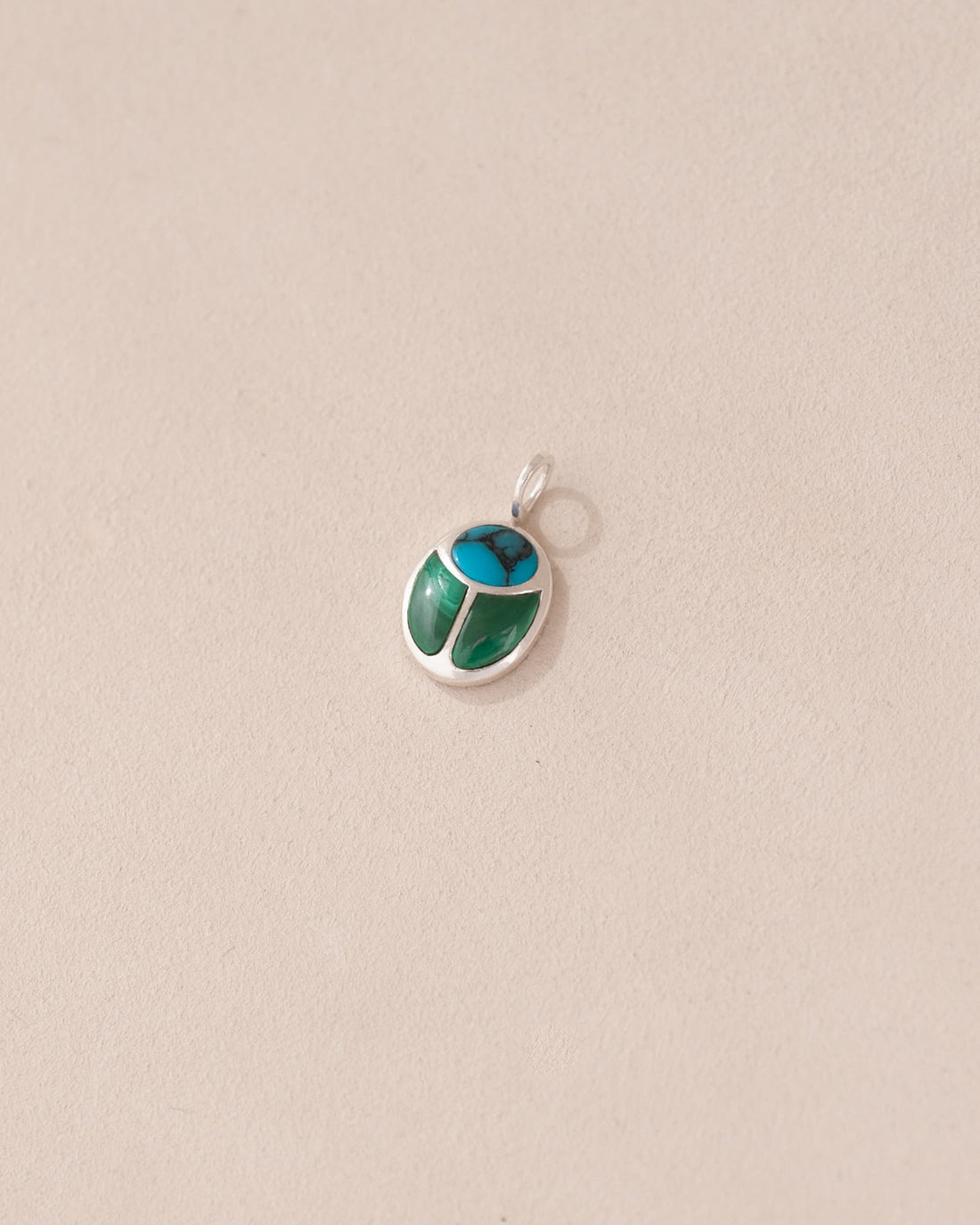 A small turquoise and malachite scarab charm set in silver, placed against a beige background.