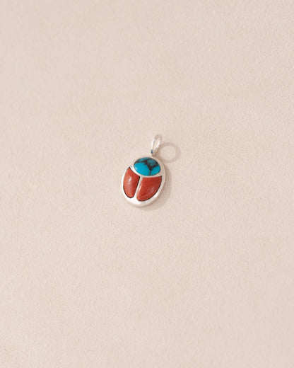 A small silver charm featuring a turquoise and red jasper design, shaped like a scarab amulet.