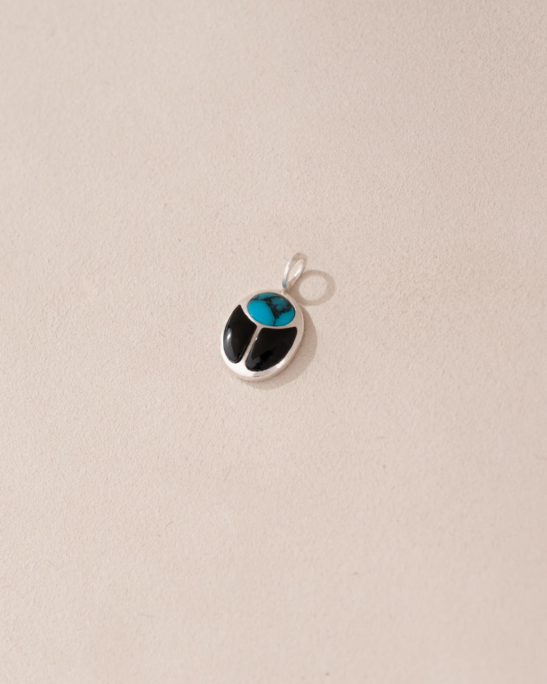 A small turquoise and onyx scarab charm in silver, displayed against a neutral background.