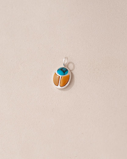 A silver charm featuring a turquoise and mookaite stone in the shape of a scarab amulet.