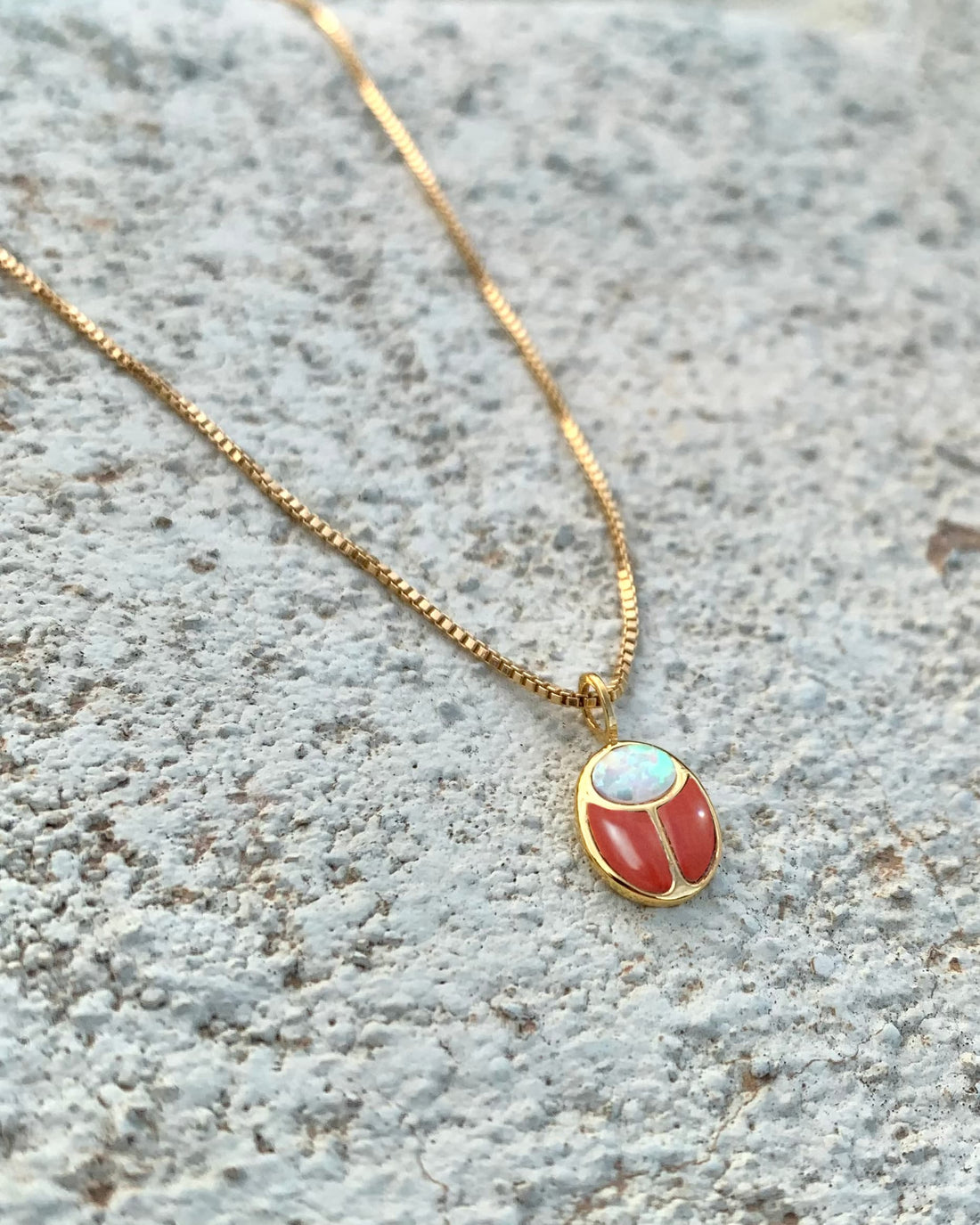 red jasper and opal gold scarab charm on gold chain on textured backgorund