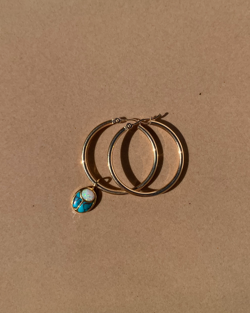 turquoise and opal charm in gold with gold hoops on a beige background
