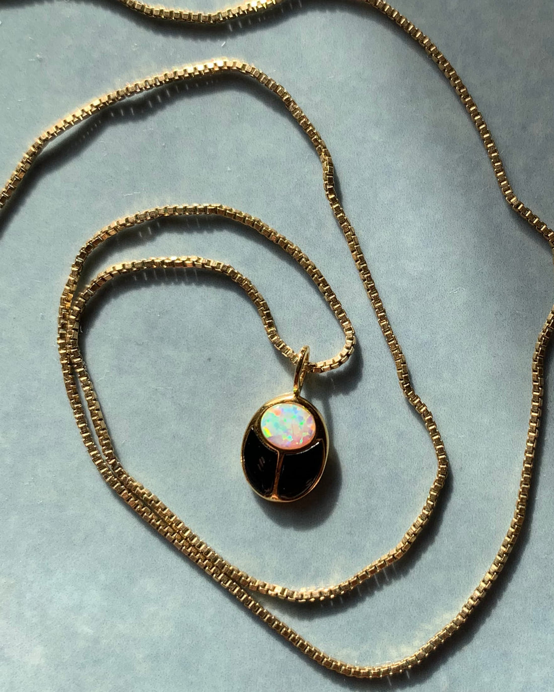 onyx and opal gold scarab on gold chain on top of blue background