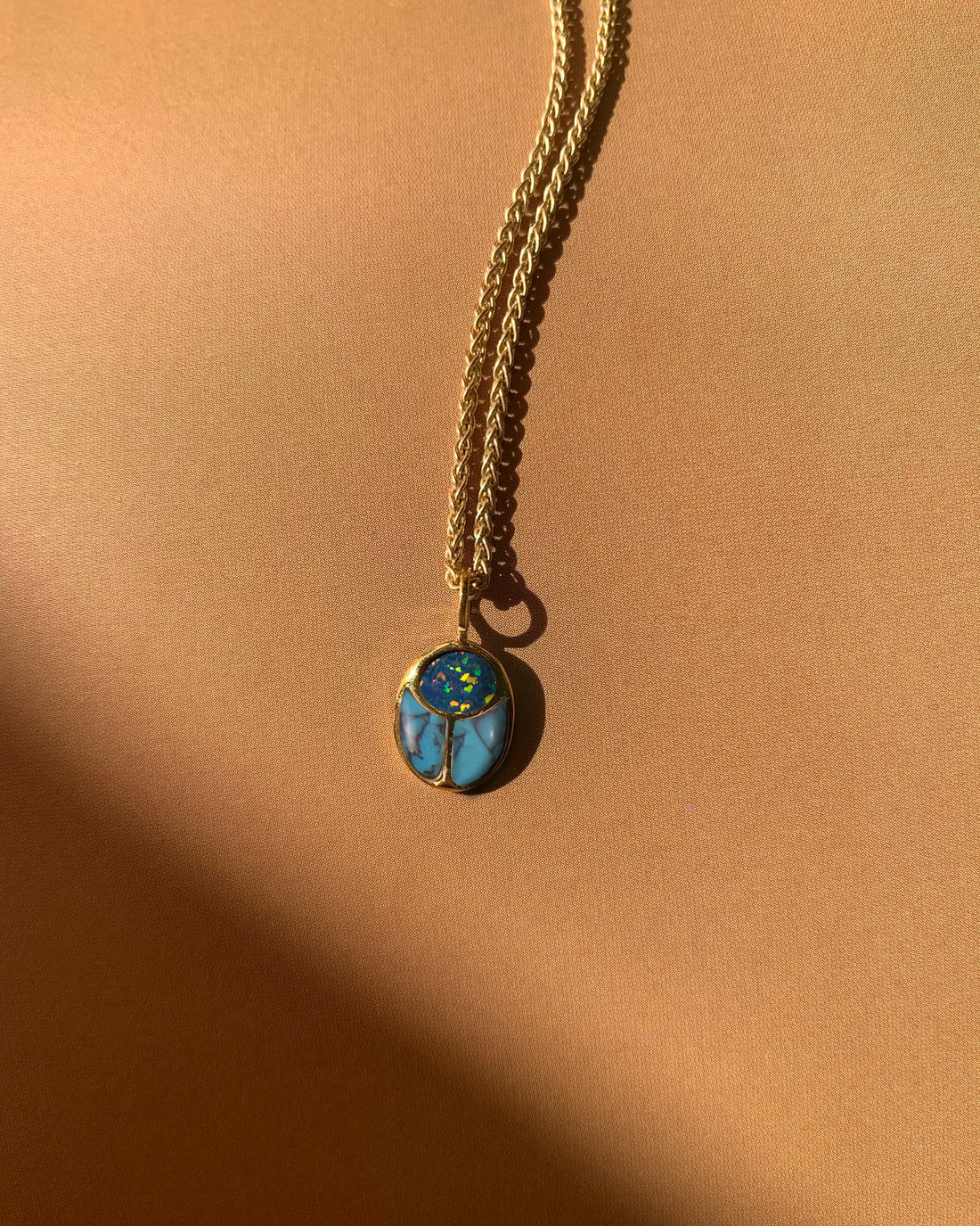 opal and turquoise scarab charm on a gold chain on a peach colored background