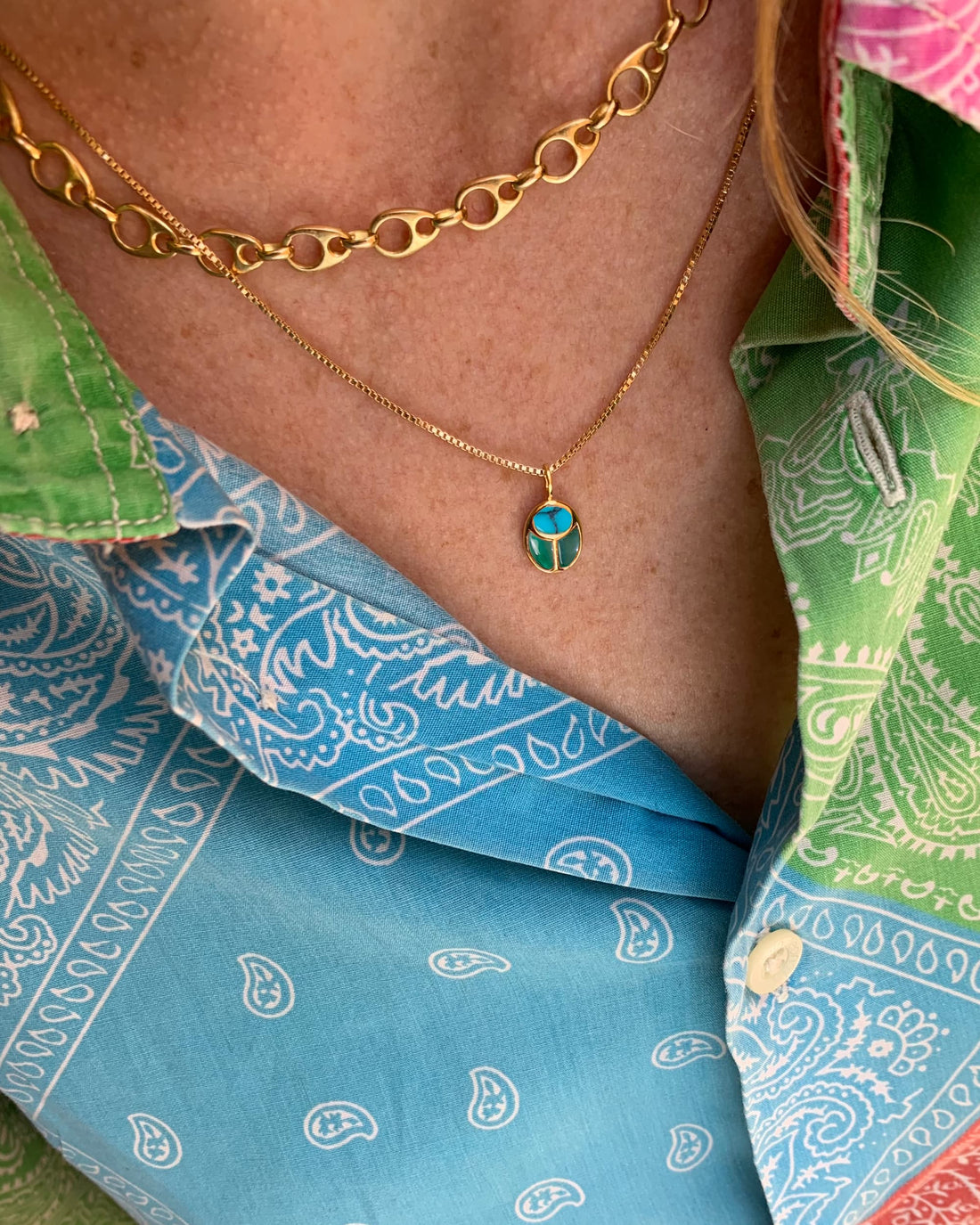 model wearing a scarab charm on a gold chain and a colorful shirt