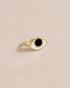A gold-colored ring with a black stone shaped like an eye, placed on a neutral background.