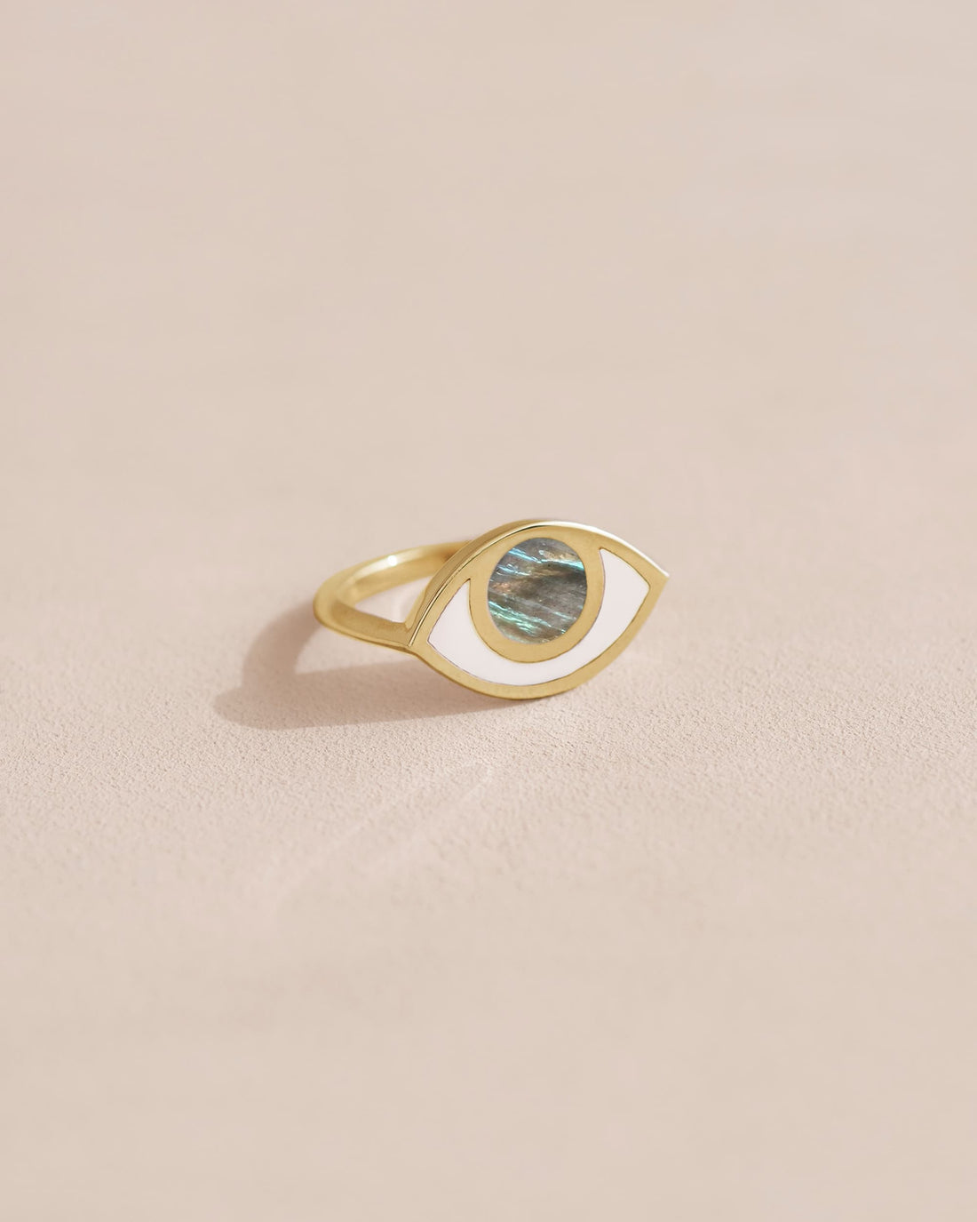 A gold ring with a labradorite stone in the shape of an eye, placed on a light background.