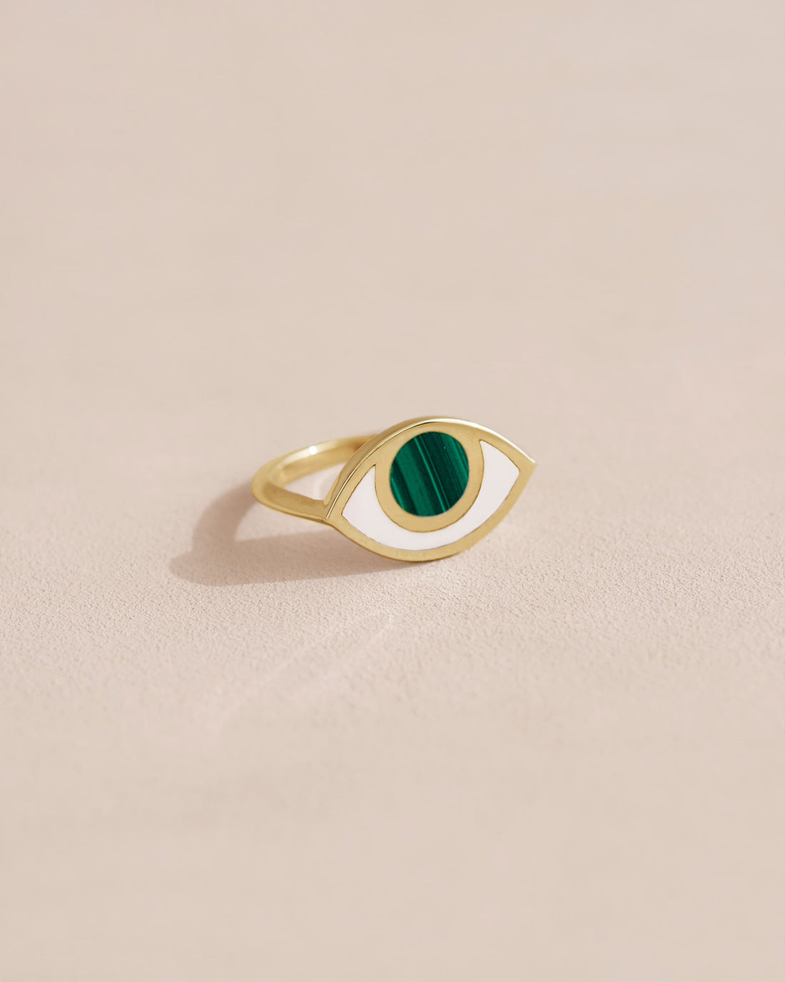 A 14K yellow gold ring with a malachite stone shaped like an eye, placed on a light background.