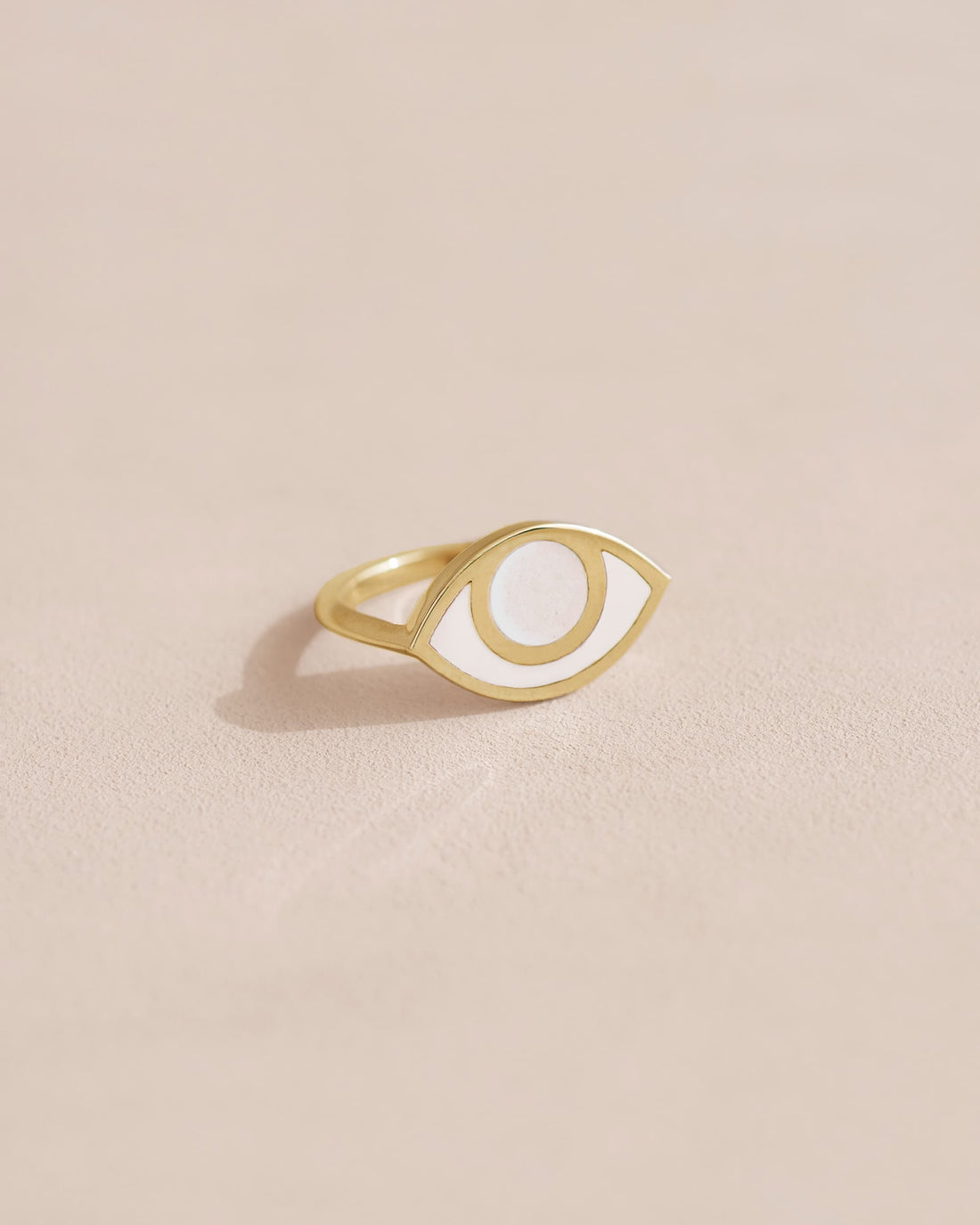 Gold ring with a white eye design on a beige background