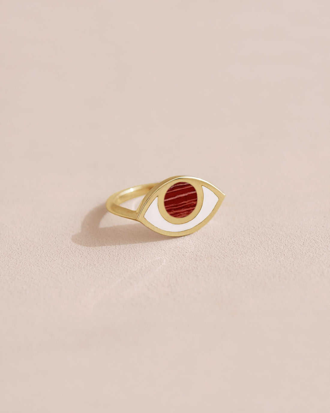 A gold ring with a jasper stone shaped like an eye set in the center, on a plain background.
